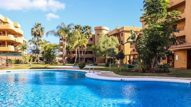 Una piscina rodeada de palmeras y edificios con balcones.