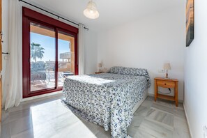 Een slaapkamer met een bed, nachtkastje, lamp, een schuifdeur en uitzicht op buiten.