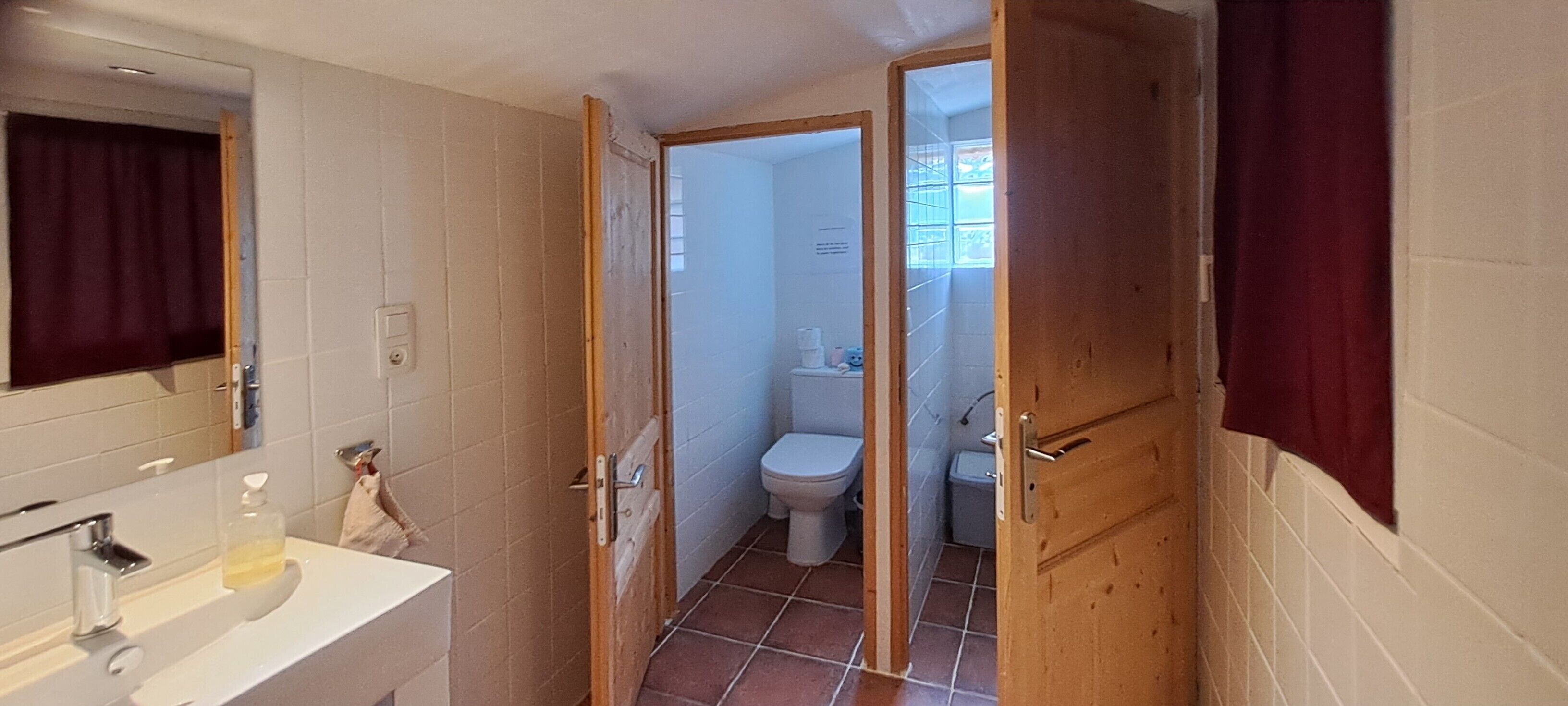 Un bagno con un lavandino bianco, uno specchio e un water visibile attraverso una porta aperta.