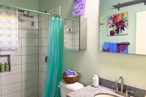 A bathroom with a shower, toilet, sink, and a basket of toiletries.