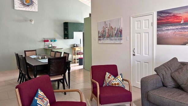 Uma sala de estar com sofá, poltrona vermelha e área de refeições com mesa e cadeiras.