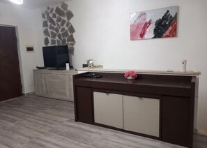 A room with a wooden floor, a dark brown console table with a vase of pink flowers, a flat-screen TV, and a stone wall decoration. - Domus acquedotto  (Roma)