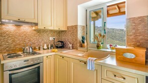 Une cuisine avec un mur de fond en briques, une cuisinière, un évier et une fenêtre donnant sur la campagne.