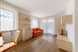 Une pièce avec un plancher en bois, un canapé rouge, un meuble en bois et un bureau avec un ordinateur.