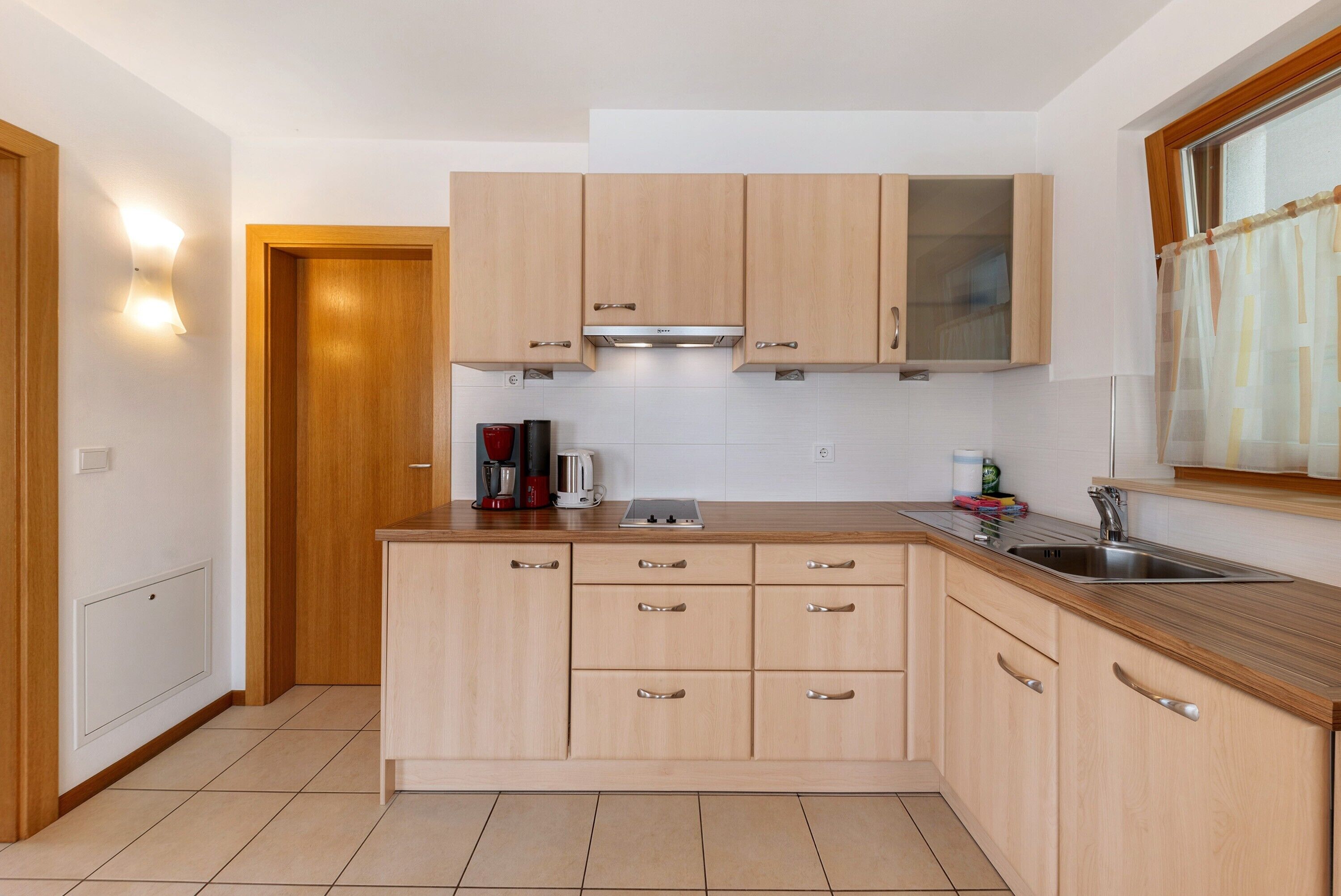 Une cuisine moderne avec des meubles en bois, un évier en acier inoxydable et une fenêtre avec un rideau.