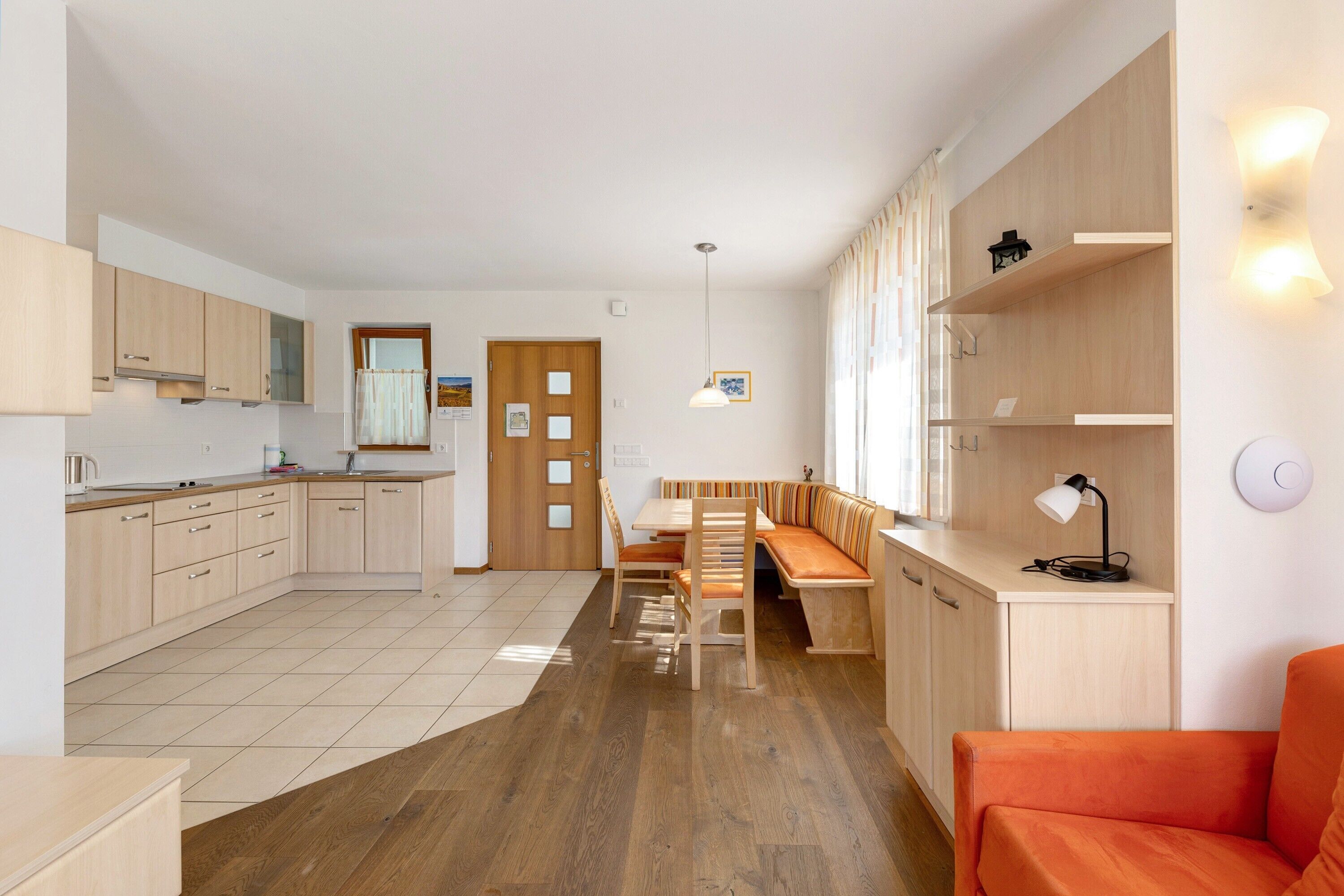 Een moderne keuken met houten kasten, een eethoek met een bank, en een heldere wandlamp.