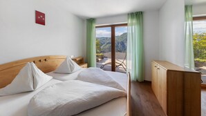 A bedroom with a wooden headboard, a bed with white linens, a wooden cabinet, and a balcony with green curtains.