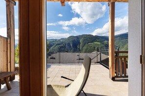 En balkon med åben udsigt over grønne bakker og en tennisbane.