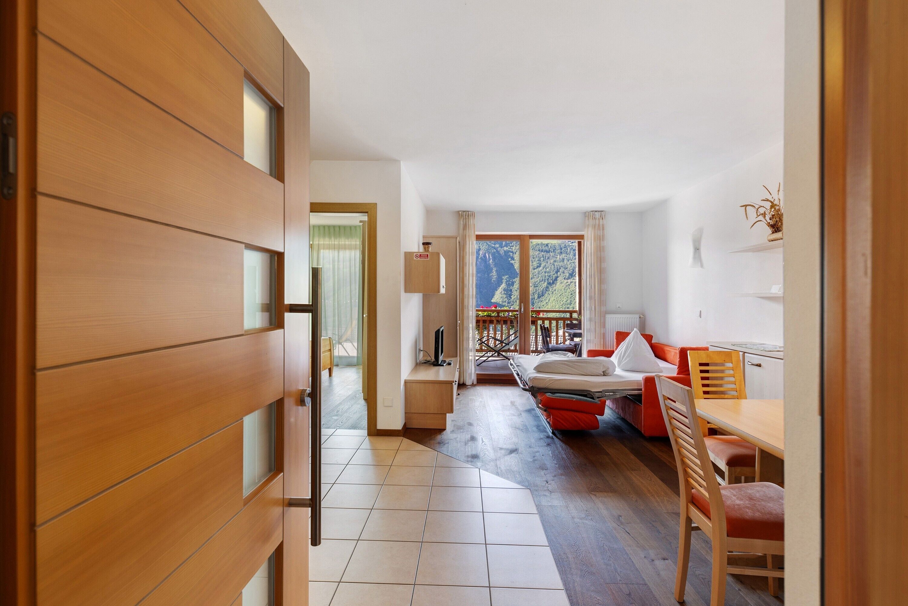 Una habitación con puerta de madera, una cama, un escritorio, una silla y vistas a un balcón.