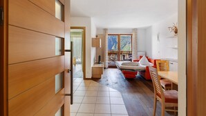 A room with a wooden door, a bed, a desk, a chair, and a view of a balcony.