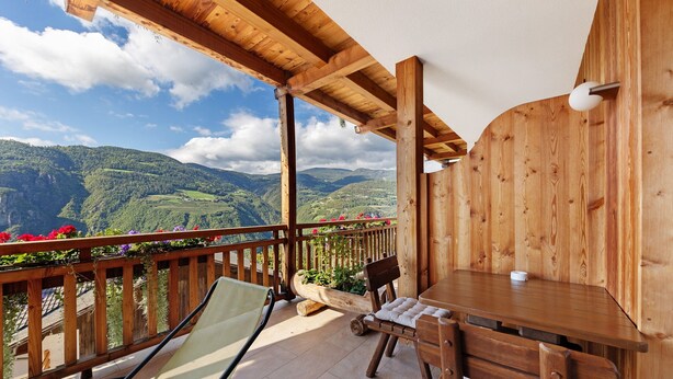 A wooden balcony with a table and chairs, overlooking a mountainous landscape.