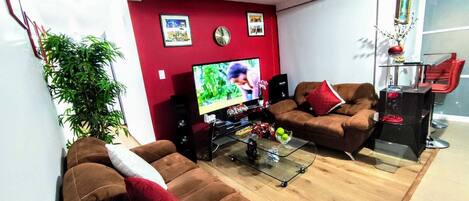 A modern living room with a red accent wall, two brown sofas, a glass coffee table, and a television.