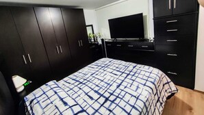 Ein Schlafzimmer mit einem Bett, einem dunklen Holzschrank, einem Fernseher und einem kleinen Schreibtisch.