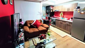 Eine moderne Küche mit Holzschränken, einem Edelstahl-Kühlschrank und einem Essbereich mit Glastisch und braunem Sofa.