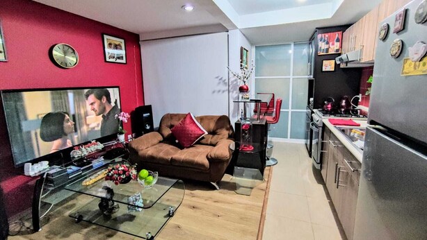 Ein kompakter Wohnbereich mit Sofa, Fernseher, Glastisch und einer Küchenzeile.