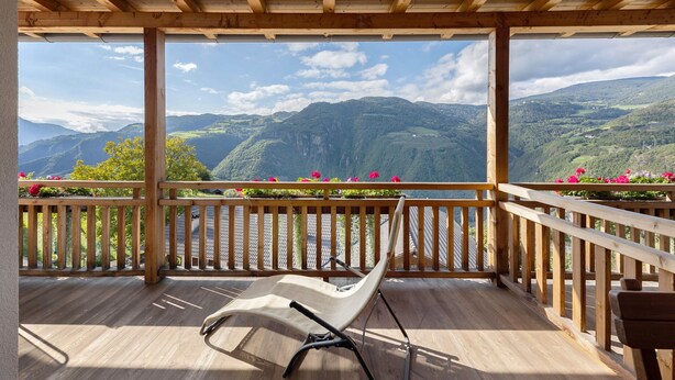 A wooden deck with a chair, wooden railings, and a view of mountains.