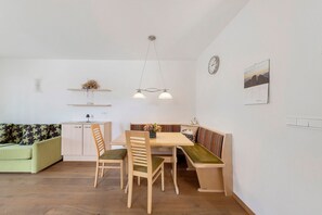 A dining area with a wooden table, chairs, and a bench. There is a light fixture above the table and a clock on the wall.