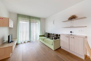 A modern room with a sofa, a small cabinet, a desk with a computer, and a window with sheer curtains.