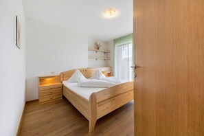 Una camera da letto con un letto di legno, comodini, un tavolino e uno scaffale a parete con una pianta, oltre a una finestra con tende.