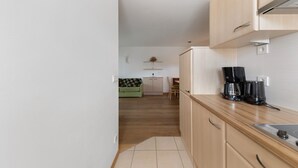 A narrow kitchen with wooden cabinets, a coffee maker, and a dining area with a green sofa.