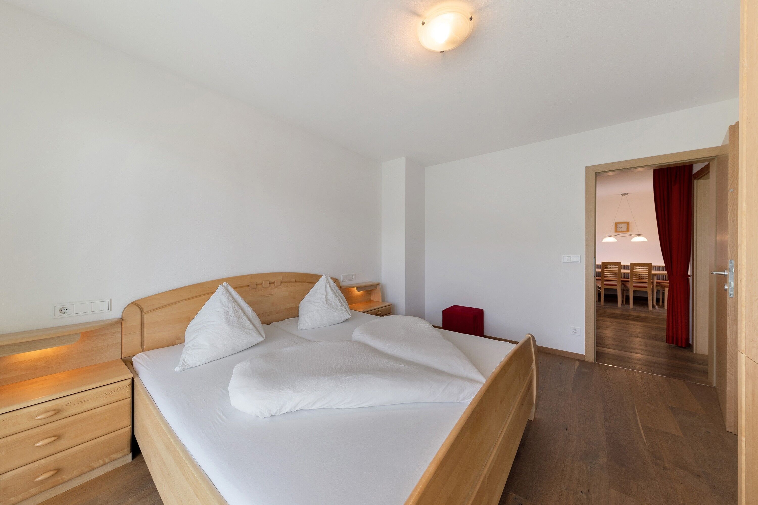 A bedroom with a wooden bed, bedside tables, a red chair, and a wooden floor.