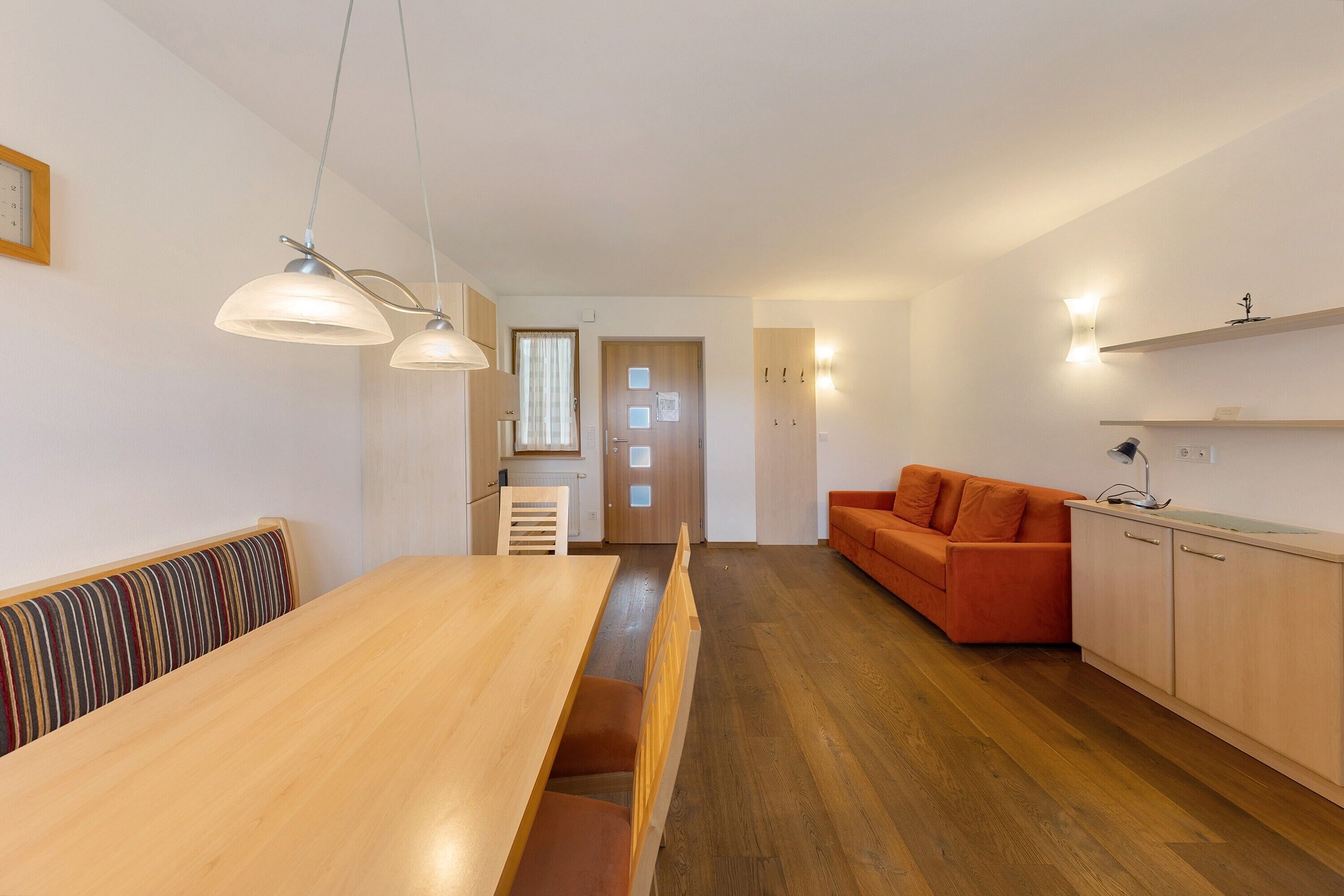 A modern kitchen with wooden cabinets, a dining table with benches, and pendant lighting.