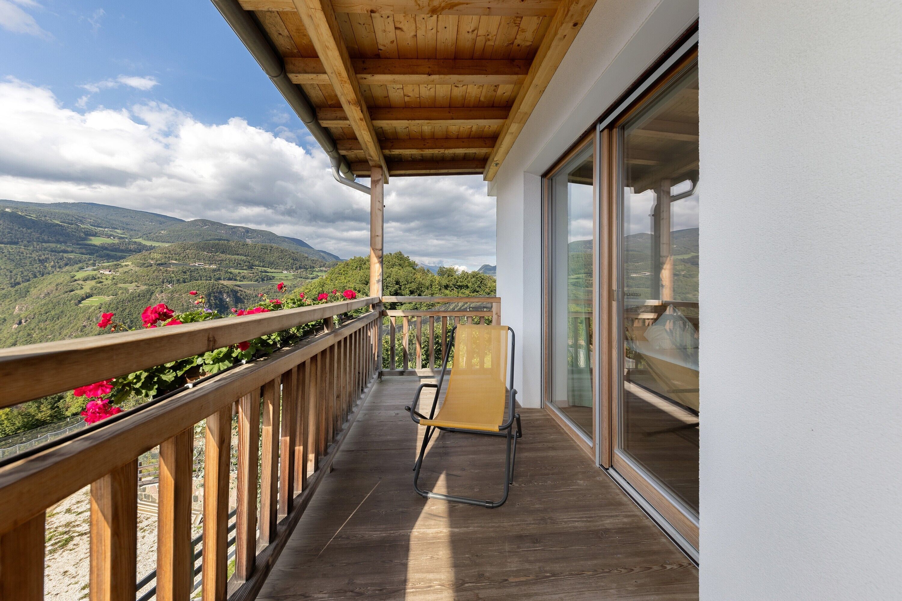 Een balkon met houten spijlen, een stoel en uitzicht op een bergachtig landschap.