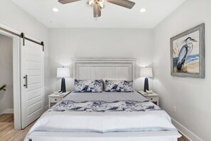 A bedroom with a bed, two bedside tables, a ceiling fan, a door, and a wall-mounted painting. - “New”Luxe Beach House HEATED PRIVATE POOL! Sleeps 10, 4 Min. walk to the Beach (Gulf Shores)