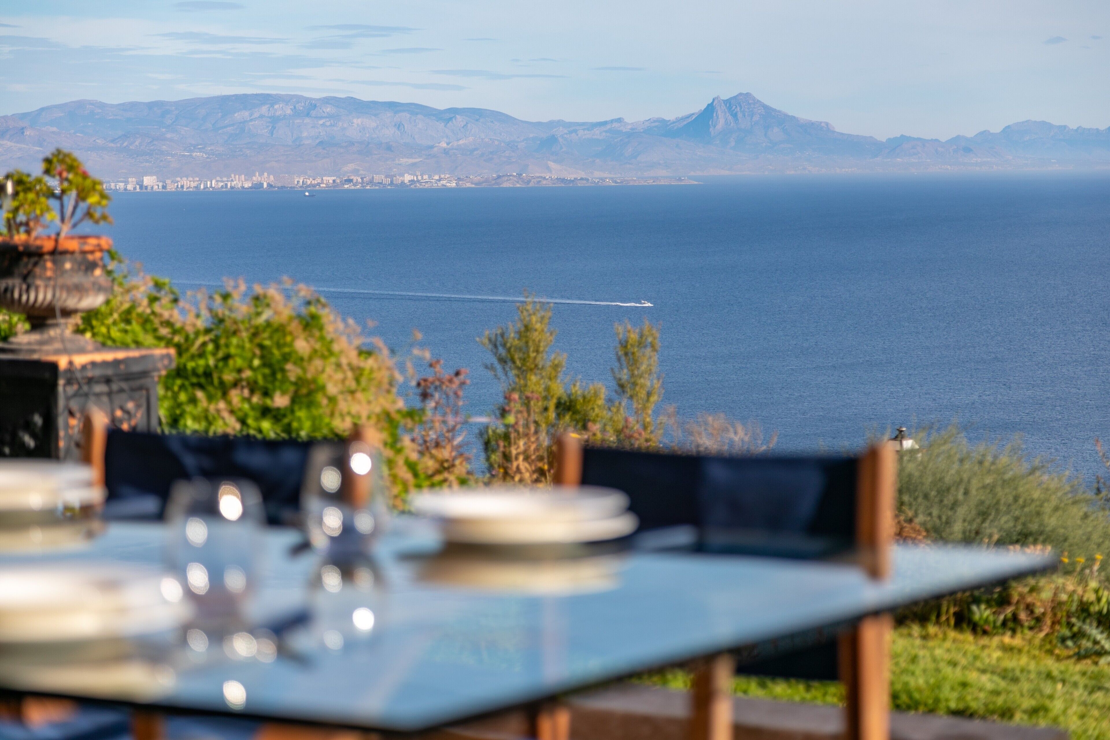 Una mesa con platos y cubiertos, con vista a un cuerpo de agua y montañas al fondo.