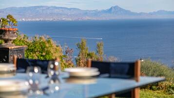 Una mesa con platos y cubiertos, con vista a un cuerpo de agua y montañas al fondo.