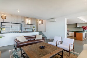 A modern living room with a brown leather sofa, white armchairs, a wooden coffee table, and a kitchen in the background. - Villa 'Almela's' with Spectacular Sea View, Wi-Fi and Air Conditioning (Santa Pola)