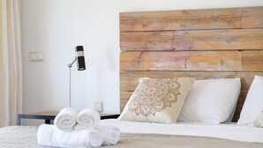 Un lit bien fait, avec des serviettes pliées, une tête de lit en bois et une lampe de chevet.