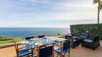 Un coin repas avec une table et des chaises en verre, offrant une vue panoramique sur l’océan.