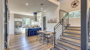 Una cocina moderna con una isla central, un área de comedor con taburetes y una escalera con barandilla de metal.