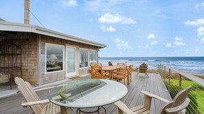 Eine Holzterrasse mit einem Glastisch und Stühlen, mit Blick auf den Ozean.