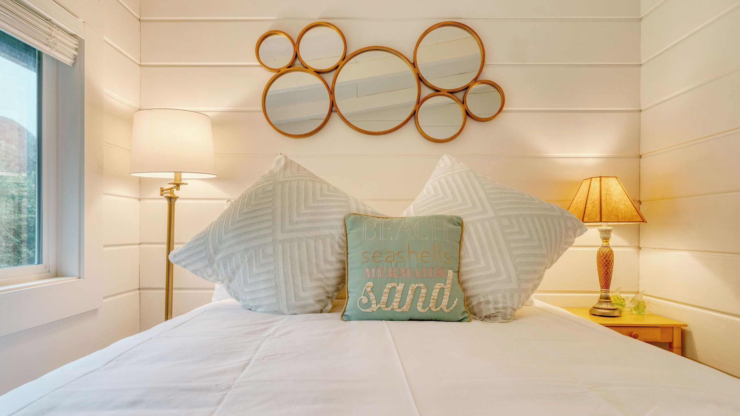 A neatly arranged bedroom with a bed, two lamps, a wall-mounted mirror, and decorative pillows.
