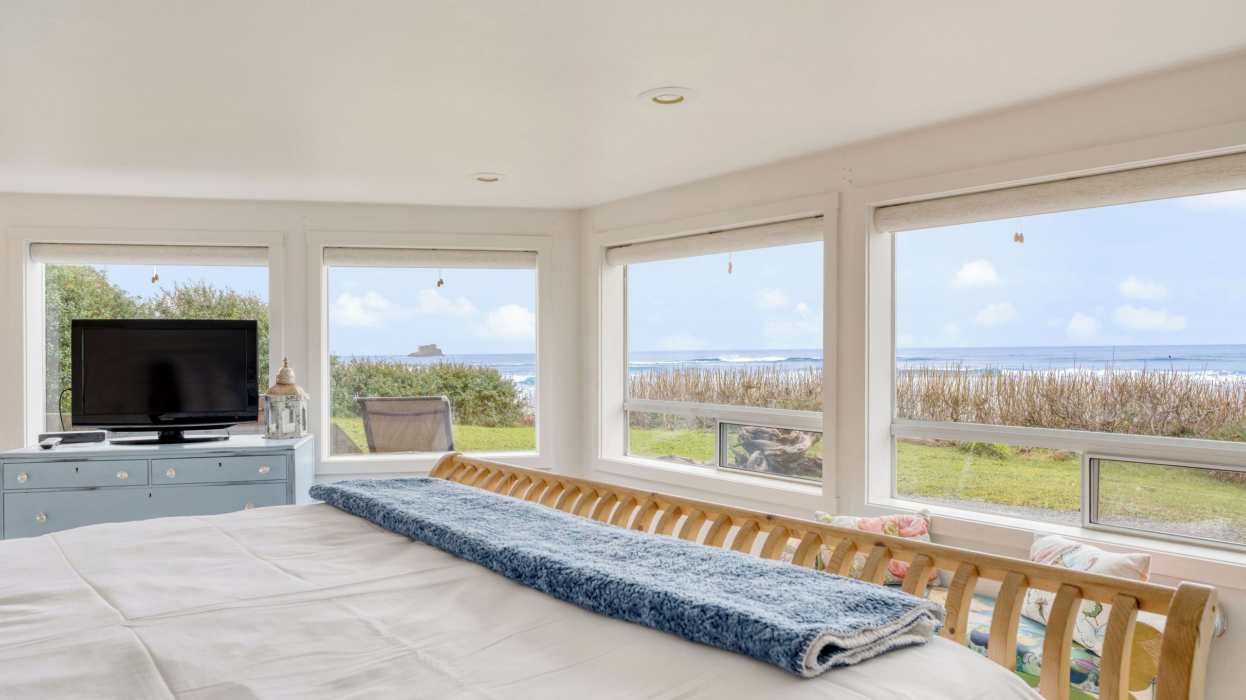 Een slaapkamer met een bed, een televisie, een dressoir en grote ramen met uitzicht op de oceaan.