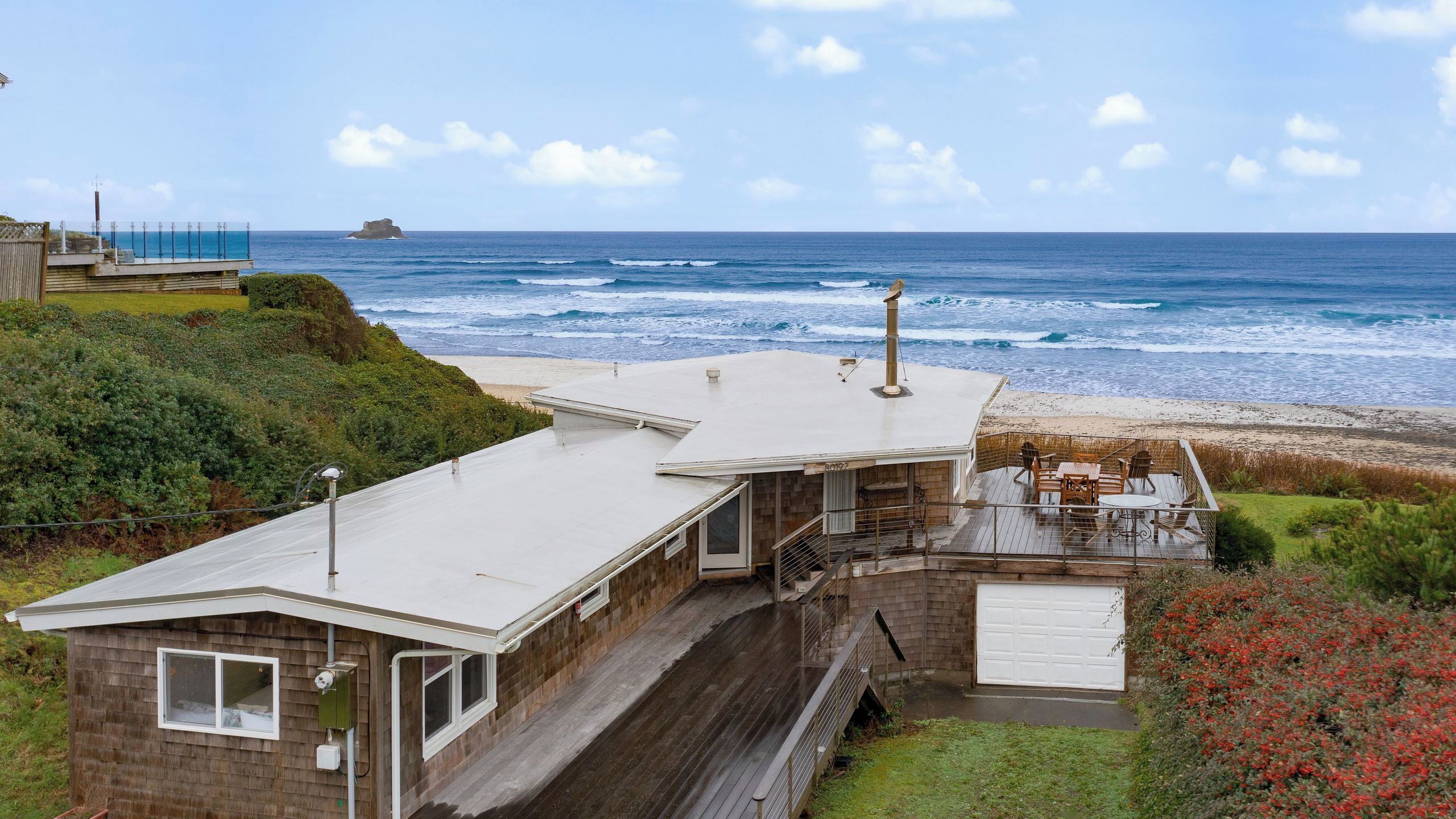 Ein Küstenhaus mit einer großen Terrasse, einer Garage und Blick auf den Ozean.