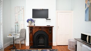 Un salon avec une cheminée, un téléviseur fixé au mur, une porte et une petite table avec une chaise.