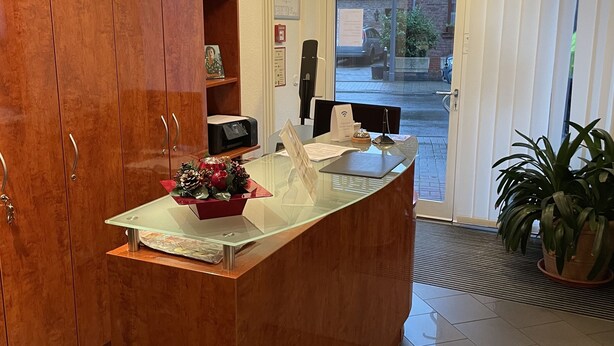 Un comptoir d’accueil avec un revêtement en bois, un plateau en verre et une petite plante placée à droite.