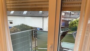 Une porte vitrée donnant sur un balcon agrémenté d’une rambarde en métal, d’une petite table et d’une chaise.