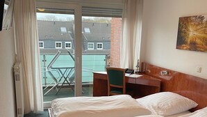 Une chambre d’hôtel avec un lit, un bureau, une chaise et une vue sur les bâtiments, visible à travers une porte vitrée.