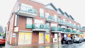 Un immeuble résidentiel à plusieurs étages, doté de balcons, d’un garage et situé dans une rue souvent mouillée.