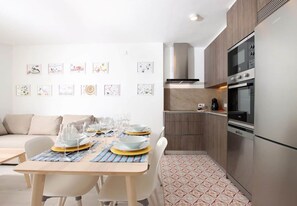 A modern kitchen with stainless steel appliances, a dining area with a table set for four, and a living area with a sofa.
