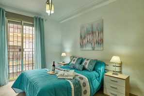 A bedroom with a bed, two bedside tables, a painting, and a view through a window with curtains.