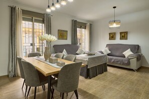 Un espace repas comprenant une table en bois, des chaises à revêtement gris, un canapé gris et un luminaire suspendu.