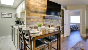 Une cuisine moderne avec un mur d’accent en pierre, un coin repas avec une table et des chaises en bois, et une vue sur une chambre.