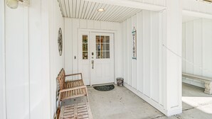 En lys facade med en træbænk, en dør med et vindue og en velkomstskilt.