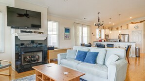 En stue med pejs, fjernsyn, sofa og et spiseområde med et køkken i baggrunden.