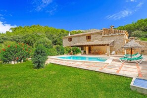 Una villa de piedra con piscina, mobiliario exterior y abundante vegetación.